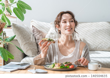 Stylish young Asian woman eating at the living room table Stylish young Asian woman eating at the living room table 140504635