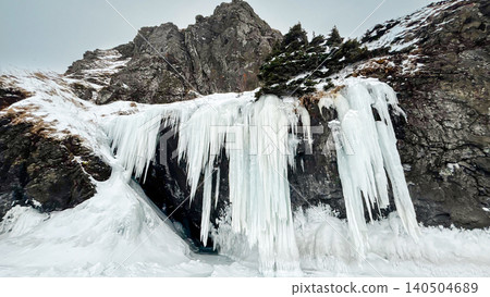 Frozen waterfall and icefall on rocky mountain cliff with deep snow and pine trees in winter 140504689