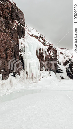 Ice waterfall and icicles on rocky cliff above frozen water in winter Ice waterfall and icicles on rocky cliff above frozen water in winter 140504690