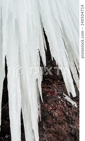 Icicles hanging from frozen cliff over dark rock. Winter ice texture background. 140504714