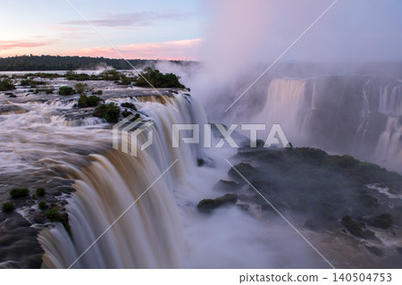 Dramatic breathtaking iguazu falls pouring water into river mist at sunset Dramatic breathtaking iguazu falls pouring water into river mist at sunset 140504753