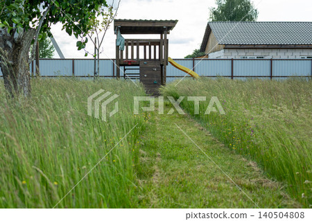 Part of a backyard lawn left uncut with high wild green grass. Landscaping negligence and lawn care theme Part of a backyard lawn left uncut with high wild green grass. Landscaping negligence and lawn care theme 140504808