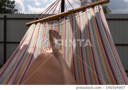 Personal perspective of feet lying in a colorful striped hammock in the backyard. Summer relaxation concept 140504907