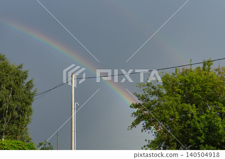 Vibrant double rainbow arching over green summer trees and power line pole Vibrant double rainbow arching over green summer trees and power line pole 140504918