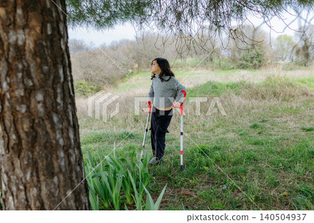 Young girl with crutches standing in a grassy field Young girl with crutches standing in a grassy field 140504937