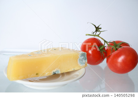 Piece of hard cheese spoiled by mold and Fresh Tomatoes on a Bright White Plate in refrigerator 140505298
