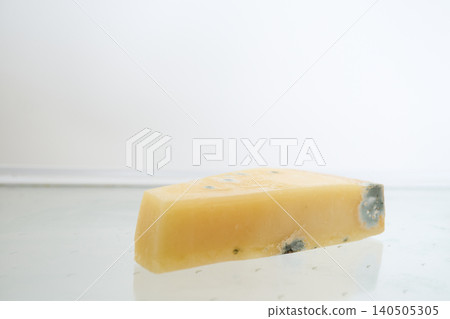 A piece of hard cheese, spoiled by mold, on an empty glass shelf of the refrigerator 140505305