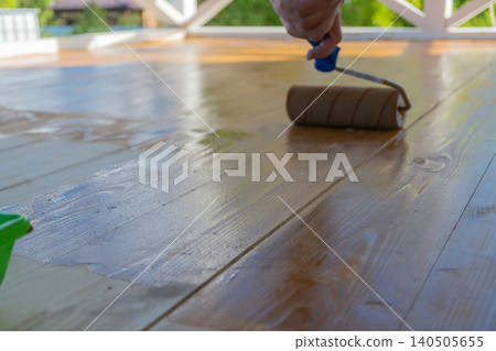 Close-up of wooden deck varnishing with roller in sunlight Close-up of wooden deck varnishing with roller in sunlight 140505655