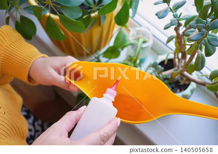 Top view of Hands holding a bottle of hydrogen peroxide over a yellow watering can Top view of Hands holding a bottle of hydrogen peroxide over a yellow watering can 140505658