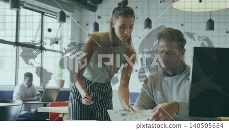 Leaning woman in green top and striped skirt, seated man reviewing printed document in office 140505684