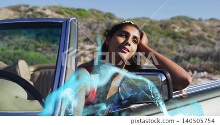 Leaning Indian woman in red top resting head, gazing at coastal dunes, with convertible blue streak 140505754