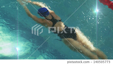 Gliding swimmer wearing blue cap dark swimsuit goggles, slicing lap pool water past red lane marker Gliding swimmer wearing blue cap dark swimsuit goggles, slicing lap pool water past red lane marker 140505773