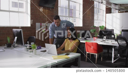 Working woman in mustard blouse and man in blue shirt leaning over laptop at loft, smartphone Working woman in mustard blouse and man in blue shirt leaning over laptop at loft, smartphone 140505800