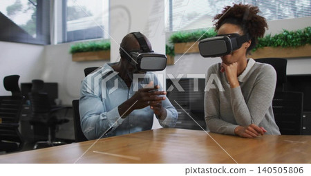 Gesturing man leaning forward, woman resting chin, wearing VR gear, office attire at long table Gesturing man leaning forward, woman resting chin, wearing VR gear, office attire at long table 140505806