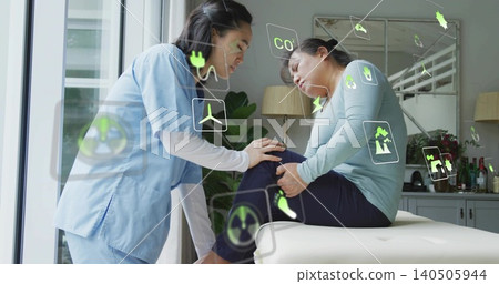Leaning nurse in light-blue scrubs examining patient knee at clinic table showing AR-green icons Leaning nurse in light-blue scrubs examining patient knee at clinic table showing AR-green icons 140505944