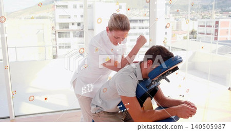 Applying pressure therapist white tunic leaning over client in grey polo, khakis on chair in clinic Applying pressure therapist white tunic leaning over client in grey polo, khakis on chair in clinic 140505987