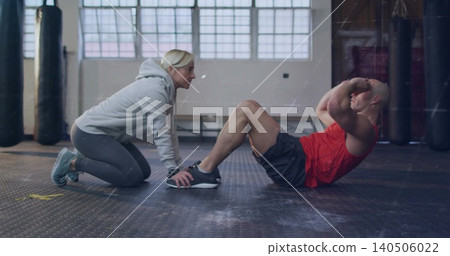 Holding feet, coach gray-hoodie supporting client red-tank doing situps in boxing gym, bags Holding feet, coach gray-hoodie supporting client red-tank doing situps in boxing gym, bags 140506022