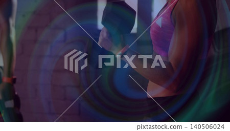 Lifting woman holding hex dumbbell at gym, wearing pink sports bra, tracker, lens rings, brick wall Lifting woman holding hex dumbbell at gym, wearing pink sports bra, tracker, lens rings, brick wall 140506024