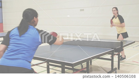 Playing two female players rallying at gym table, blue shirt, yellow skirt, red paddles, white ball Playing two female players rallying at gym table, blue shirt, yellow skirt, red paddles, white ball 140506108