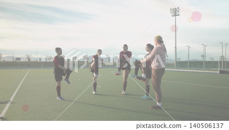 Stretching five women athletes and coach balancing, pulling knees on synthetic turf, maroon jerseys Stretching five women athletes and coach balancing, pulling knees on synthetic turf, maroon jerseys 140506137