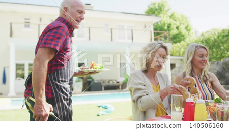 Serving senior man wearing red-black plaid shirt and striped apron holding plate and tongs poolside Serving senior man wearing red-black plaid shirt and striped apron holding plate and tongs poolside 140506160