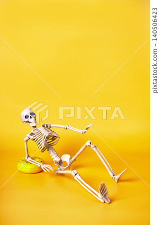 Playful Skeleton Relaxing with a Colorful Toy on a Vibrant Yellow Background Playful Skeleton Relaxing with a Colorful Toy on a Vibrant Yellow Background 140506423