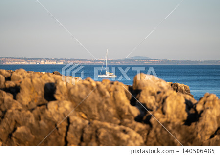 Sailboat journeying across calm blue waters near rocky coastline at sunset Sailboat journeying across calm blue waters near rocky coastline at sunset 140506485