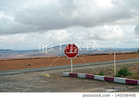 A stop sign stands in a rural area of Morocco with a vast, scenic backdrop of mountains. 140506490