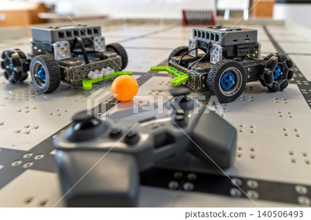 Two robots navigate a grid on the table, engaging in a fun activity with a controller nearby. 140506493