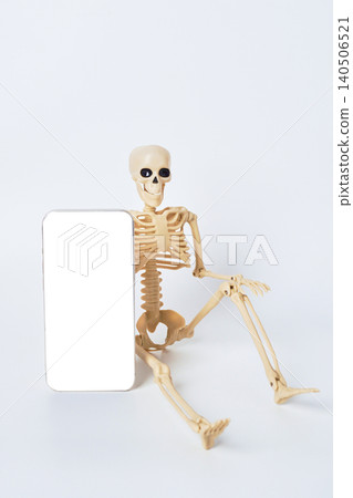 Skeleton Figure Propped Against Blank Smartphone in a Bright, Minimalist Studio Setting Skeleton Figure Propped Against Blank Smartphone in a Bright, Minimalist Studio Setting 140506521