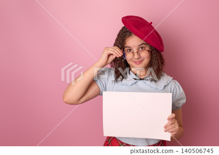 Girl in a Red Beret and Glasses Holding a Blank White Sheet Against a Pink Background Girl in a Red Beret and Glasses Holding a Blank White Sheet Against a Pink Background 140506745