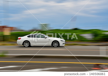 鏡頭緩緩移動,拍攝一輛白色雙門轎車行駛在郊區的景象。 鏡頭緩緩移動,拍攝一輛白色雙門轎車行駛在郊區的景象。 140506861