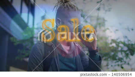 Man with dreads in hoodie jacket backpack sipping takeaway coffee on street, with neon Sale overlay 140506954