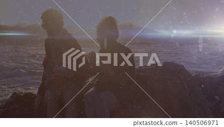 Sitting family group wearing jackets holding wrapped baby on rock outcrop by ocean waves lens flare Sitting family group wearing jackets holding wrapped baby on rock outcrop by ocean waves lens flare 140506971