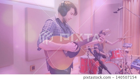 Playing guitarist in checked shirt, headphones, tracking acoustic guitar in studio, red drum kit Playing guitarist in checked shirt, headphones, tracking acoustic guitar in studio, red drum kit 140507154