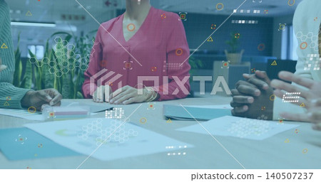 Reviewing team in pink blouse and green sweater studying charts at table with digital overlay Reviewing team in pink blouse and green sweater studying charts at table with digital overlay 140507237