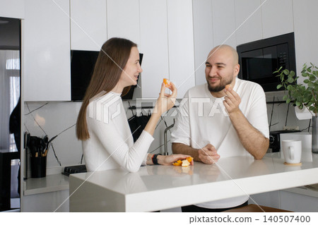 Cheerful couple having fun eating fruit and drinking coffee in domestic kitchen at home Cheerful couple having fun eating fruit and drinking coffee in domestic kitchen at home 140507400