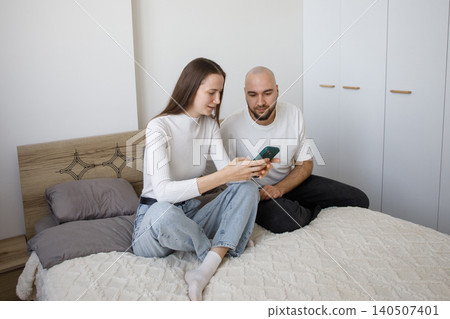 Young woman holding smartphone and sitting with man in modern apartment watching video and relaxing. Young woman holding smartphone and sitting with man in modern apartment watching video and relaxing. 140507401