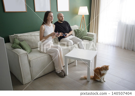Cute man and woman playing game by joysticks on sofa at home Cute man and woman playing game by joysticks on sofa at home 140507404