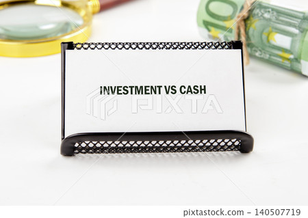 A display shows the phrase investment vs cash with tools for finance and stacks of currency nearby on a plain table surface A display shows the phrase investment vs cash with tools for finance and stacks of currency nearby on a plain table surface 140507719