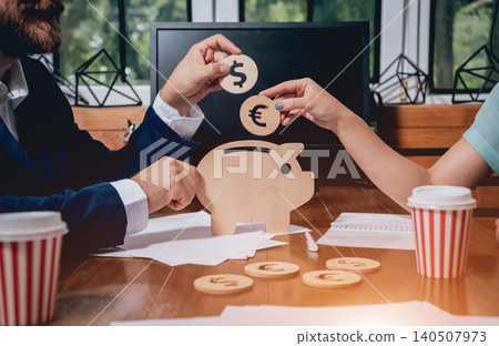 A businessman with a bank employee holds a coins under a wooden pig. Money box. Collecting money with earning bank. A businessman with a bank employee holds a coins under a wooden pig. Money box. Collecting money with earning bank. 140507973