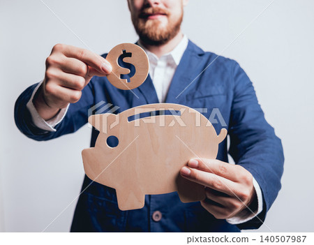 Businessman holds a coin under wooden piggy. Money box. Collecting money with earning bank. Businessman holds a coin under wooden piggy. Money box. Collecting money with earning bank. 140507987