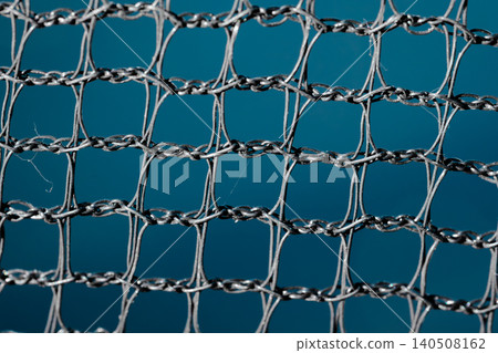 Detailed close up of a twisted metallic mesh with repeating square openings, showing a textured wire pattern against a solid blue background Detailed close up of a twisted metallic mesh with repeating square openings, showing a textured wire pattern against a solid blue background 140508162