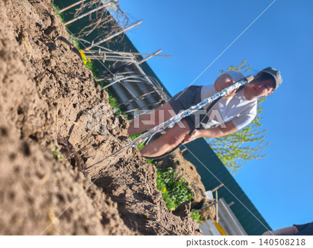 Person watering freshly tilled garden soil with a hose, nurturing young vegetable seedlings for healthy growth under a clear blue sky in a rural home garden setting. Person watering freshly tilled garden soil with a hose, nurturing young vegetable seedlings for healthy growth under a clear blue sky in a rural home garden setting. 140508218