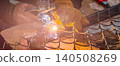 Worker wearing protective gloves performing arc welding on a metal fence outdoors, generating bright sparks and smoke, representing industrial work, repair, and craftsmanship. 140508269