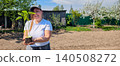 Woman smiling and holding a healthy green seedling with roots ready for planting in a prepared garden plot, symbolizing gardening, growth, and sustainable living during spring. 140508272