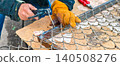 Welder's gloved hands operating an arc welding torch to join metal wire mesh for chain-link fence construction or repair, highlighting skilled, safe industrial craftsmanship. 140508276