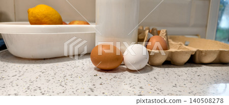 Eggs, milk, and lemon showcasing essential farm products on a speckled countertop, representing wholesome ingredients for cooking and healthy breakfast meals in a kitchen setting. 140508278