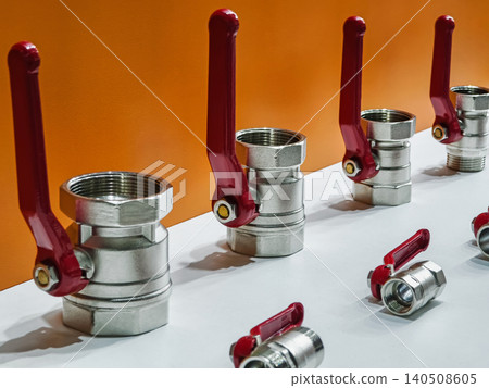Metal valves and fittings displayed on a white table against an orange background for plumbing and industry purposes Metal valves and fittings displayed on a white table against an orange background for plumbing and industry purposes 140508605