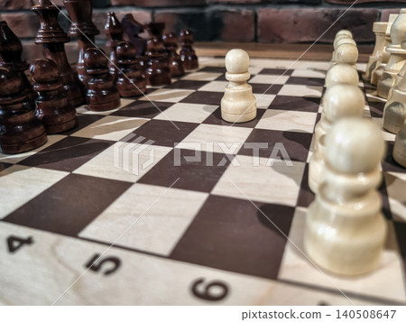 Chess game is taking place with pieces lined up on the board showing the start of a match in a warm indoor space 140508647